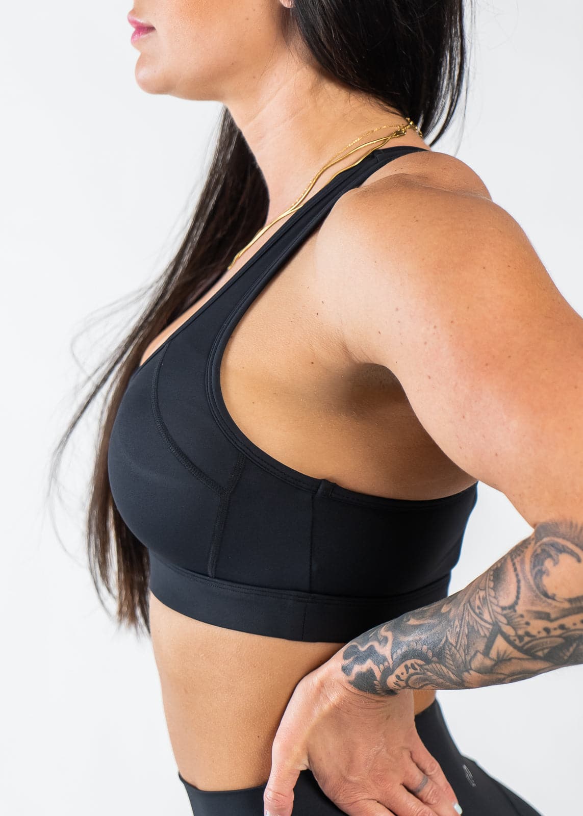 Waist Up Side View with Hand on Lower Back Wearing Empowered Laced Back Sports Bra | Black