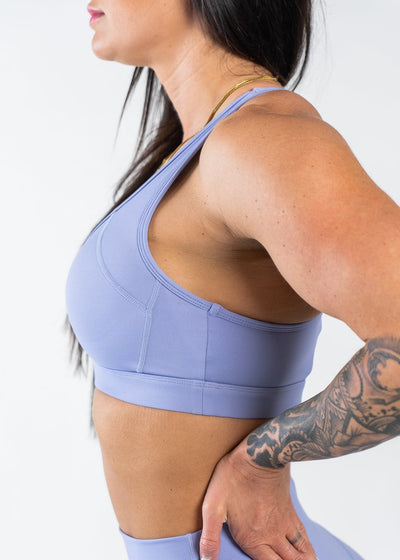Waist Up Side View with Hand on Lower Back Wearing Empowered Laced Back Sports Bra | Periwinkle