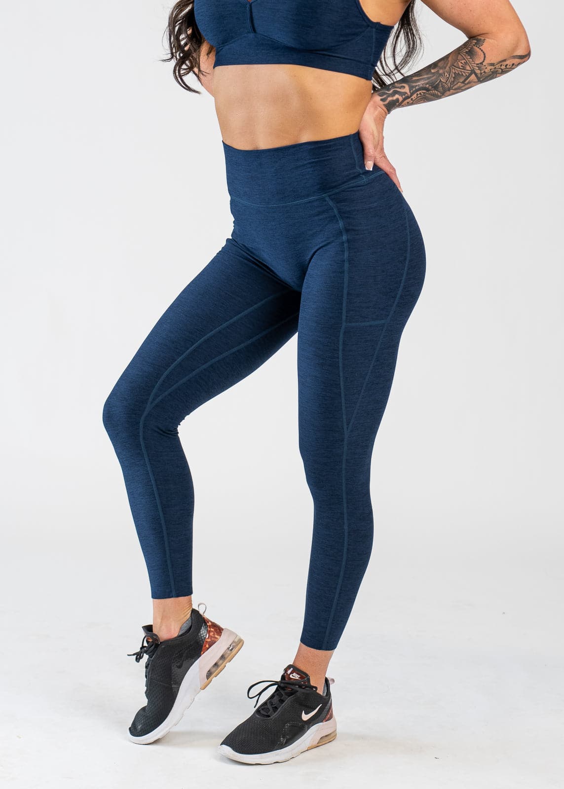 Chest Down 3/4 Front View With One Hand on Lower Back Wearing Dream Leggings With Pockets | Deep Blue