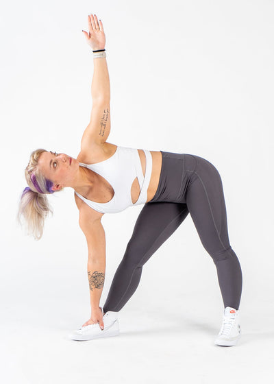 Full Body Front View Woman Bent to the Side with One Arm Touching the Ground and the Other in the Air Wearing Empowered Leggings x FIT OPS | Grey